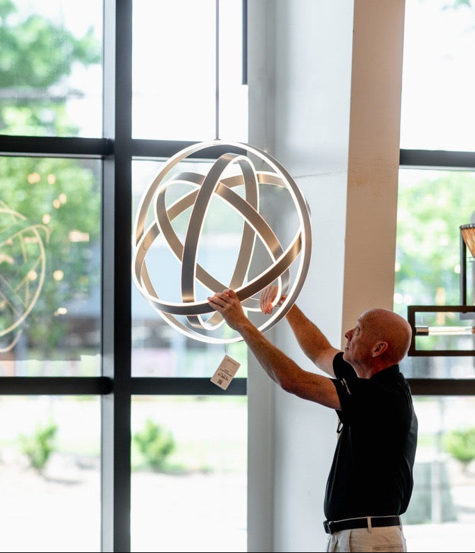 Person adjusting a decorative sphere in a modern indoor setting with large windows.
